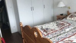 A bedroom with a wooden bed, a white wardrobe, a bedside table with a lamp, and a patterned bedspread. - Ritschis Home Appartement/Fewo, Dusche, WC, 4-Bettwohnung Ritschis Home by Interhome (Arosa)