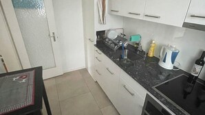 A compact kitchen with white cabinets, a black countertop, a sink, a stove, and a dining table with chairs. - Ritschis Home Appartement/Fewo, Dusche, WC, 4-Bettwohnung Ritschis Home by Interhome (Arosa)