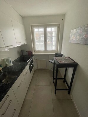 A compact kitchen with white cabinets, a black countertop, a window with bars, and a small table with a placemat. - Ritschis Home Appartement/Fewo, Dusche, WC, 4-Bettwohnung Ritschis Home by Interhome (Arosa)