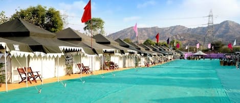 A row of tents with a swimming pool in the foreground and mountains in the background.