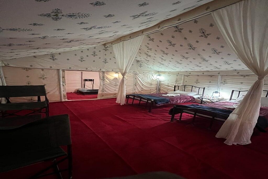 A tented room with a red carpet, two beds, a table, and a chair.