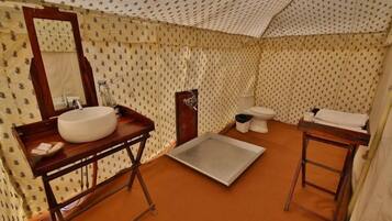 A compact bathroom with a wooden vanity, a large mirror, a sink, a toilet, and a small table with a towel.