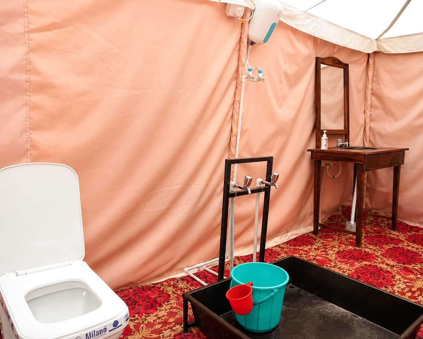 Una habitación con tienda de campaña, un inodoro, un lavamanos, un espejo y un cubo.