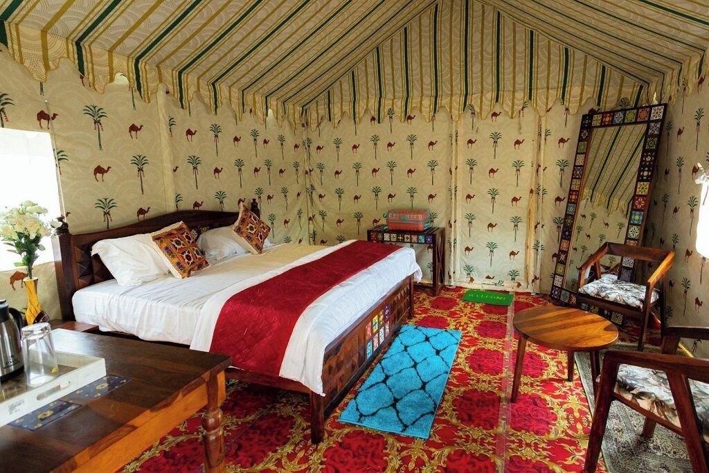 A room with a bed, a wooden table, a chair, and a mirror on the wall.