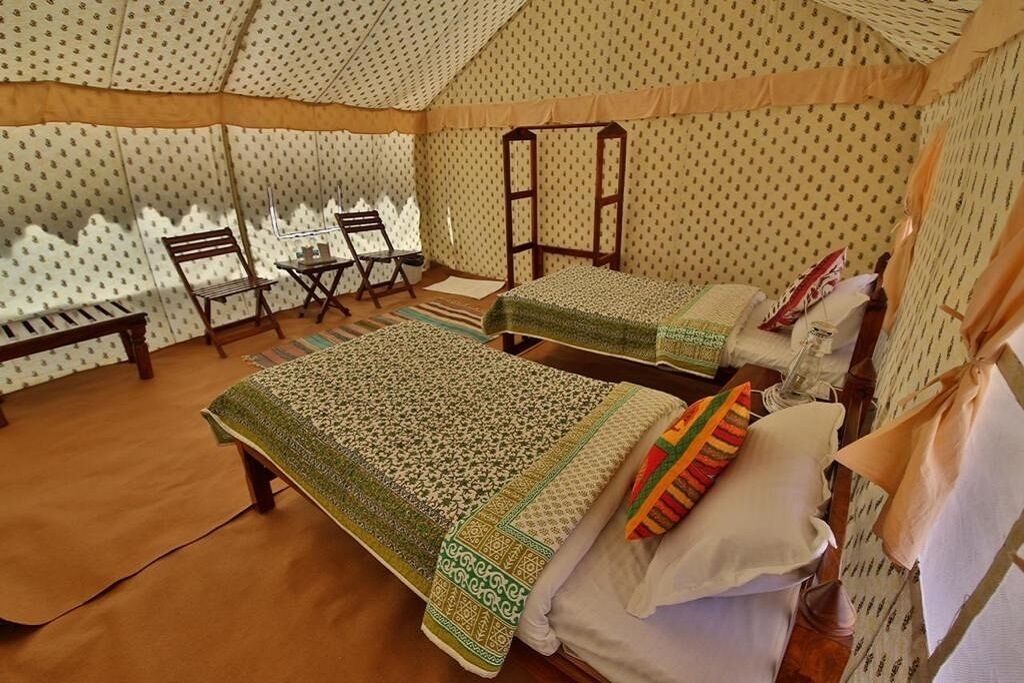 A tented room with two beds, a bench, and a small table.