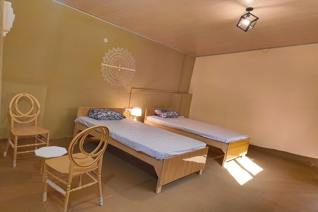 Et værelse med to senge i træ, en stol, en vægdekoration og en loftlampe.