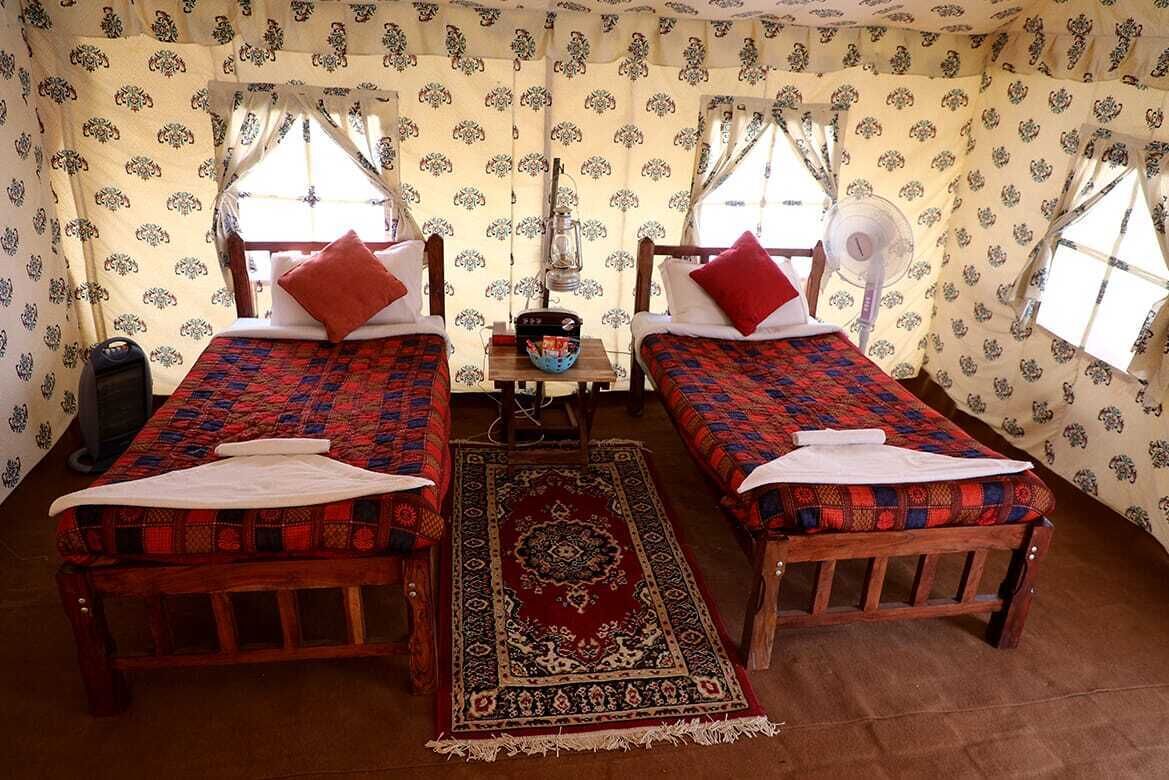 A room with two beds, a small table, and a fan.