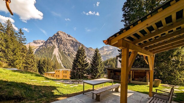 A wooden pergola with benches, a stone patio, and a mountain backdrop. - Pradella Garten by Arosa Holiday Appartement/Fewo, Dusche oder Bad, WC, 7-Bettwo by Interhome (Arosa)