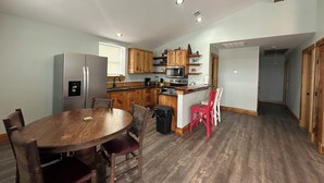 A kitchen with wooden cabinets, a stainless steel refrigerator, and a dining area with a wooden table and chairs.