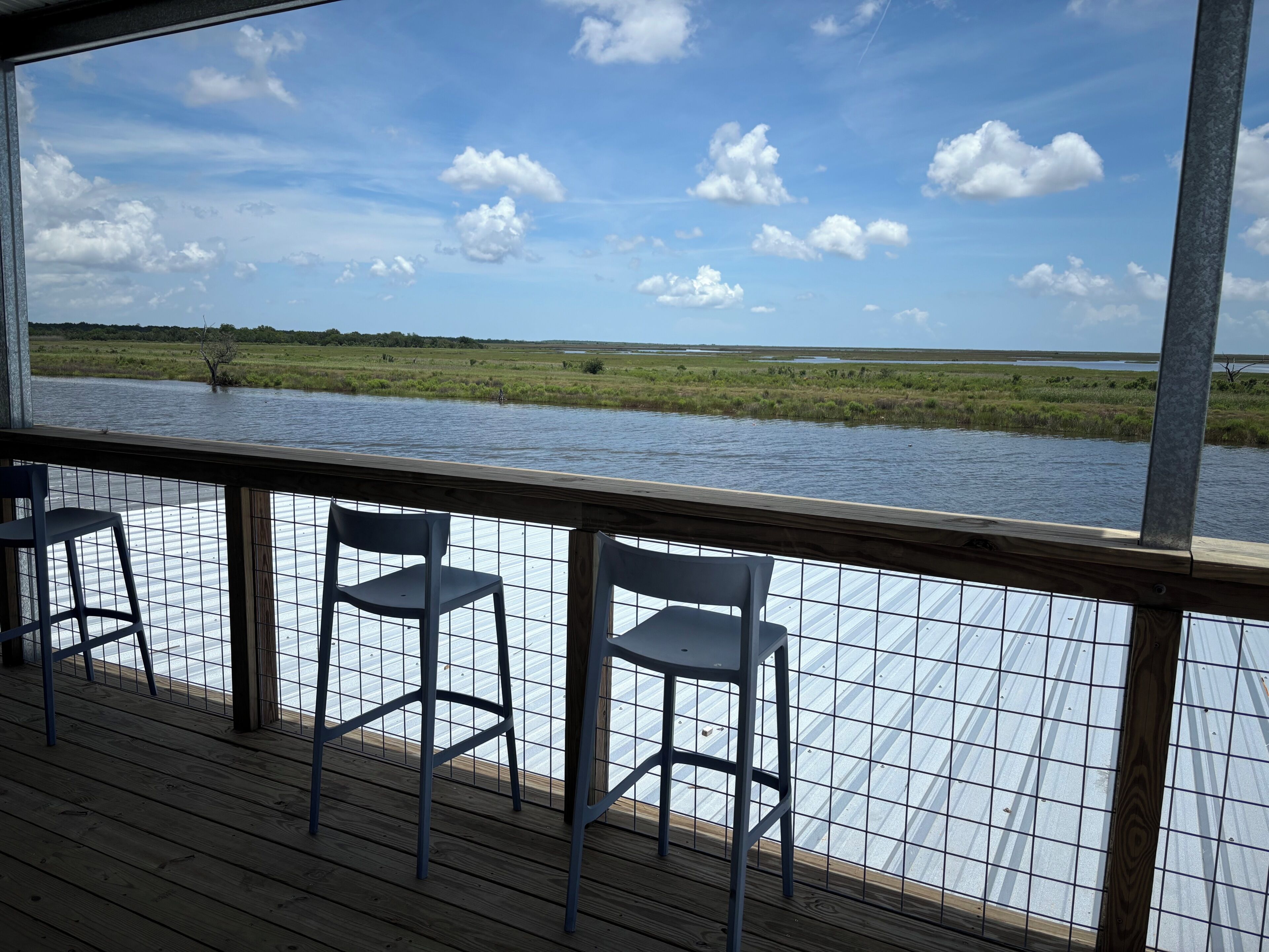 Eine Terrasse mit Stühlen mit Blick auf ein Gewässer und eine grüne Landschaft.