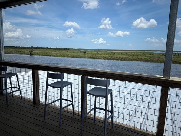 A deck with chairs overlooking a water body and grassy landscape.