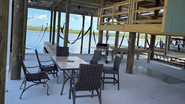 A covered outdoor area with wooden beams, a table with chairs, and a grill.