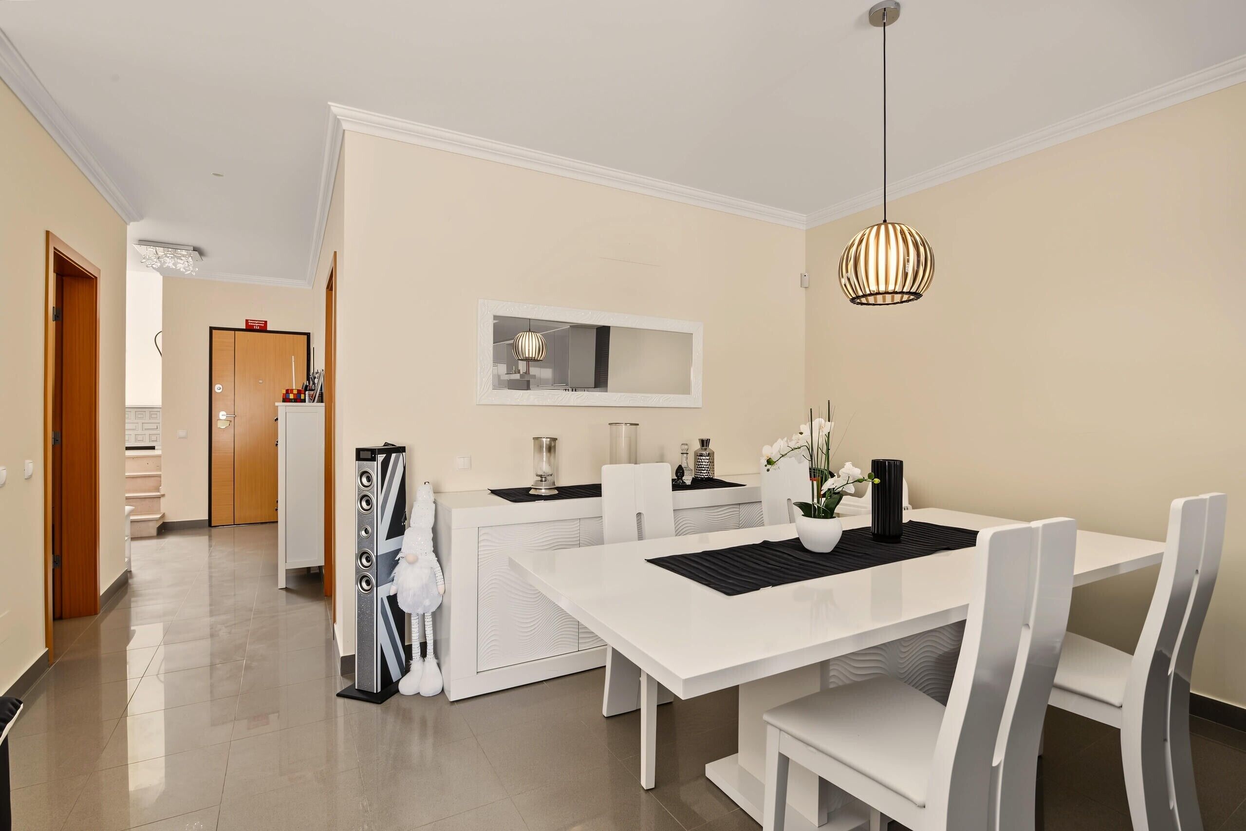 A modern dining area with a white table, chairs, and a hanging light fixture.