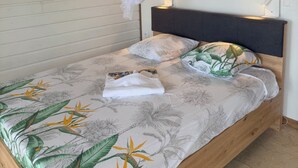 Een bed met hemel, twee wandlampen en een beddeken met een tropisch bladpatroon.