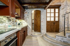 Une cuisine étroite aux murs en pierre, avec des armoires en bois et une grande porte en bois.