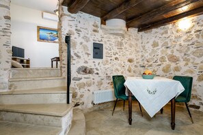 Une pièce aux murs de pierre, avec une table, des chaises et un escalier.