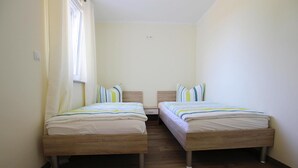 Una stanza con due letti in legno, una finestra con tende e un interruttore a parete.
