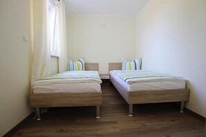 A small, clean room with two wooden beds, a window with curtains, and a light switch on the wall. - Appartement Hafenflair am Plauer See (Plau am See)