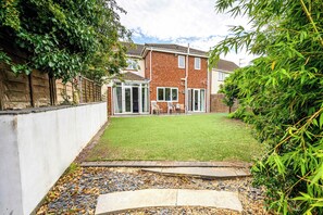 A residential backyard with a lawn, a patio with outdoor furniture, and a brick house. - Howard Road Sleeps 7 -5 Bedrooms | Parking |Garden (Bristol)