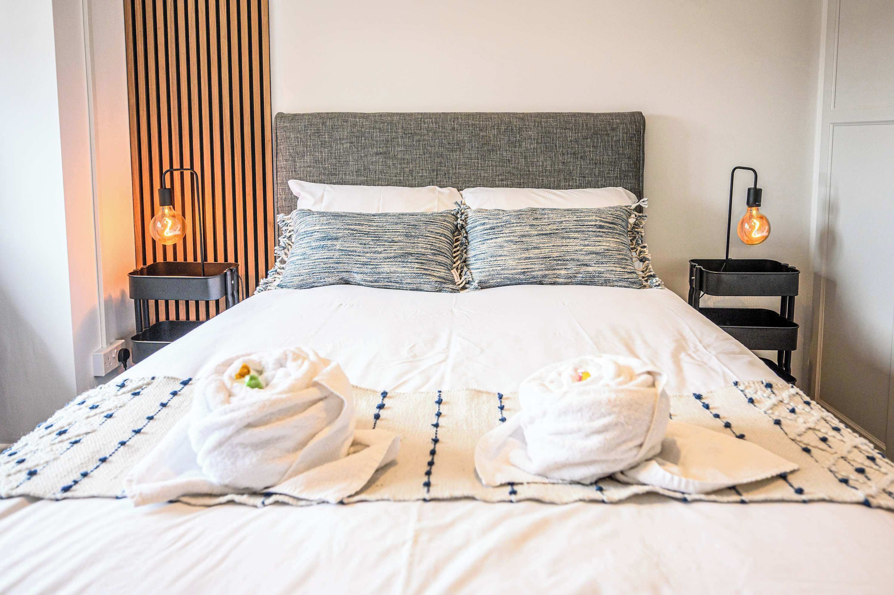 A hotel room with a bed, two pillows, two bedside tables, and two wall-mounted lamps.