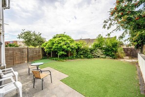 A backyard with artificial grass, a wooden fence, and a tree with purple flowers. - Howard Road Sleeps 7 -5 Bedrooms | Parking |Garden (Bristol)