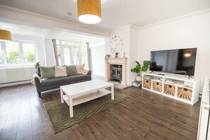 A modern living room with a sofa, coffee table, TV, fireplace, and large windows. - Howard Road Sleeps 7 -5 Bedrooms | Parking |Garden (Bristol)