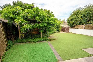 A well-maintained backyard with a grassy lawn, a wooden fence, and a variety of green shrubs and flowering plants. - Howard Road Sleeps 7 -5 Bedrooms | Parking |Garden (Bristol)