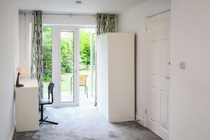 A room with a desk, chair, and a view of a garden through a glass door. - Howard Road Sleeps 7 -5 Bedrooms | Parking |Garden (Bristol)