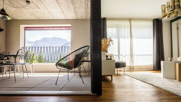 En moderne stue med balkon, trægulv og spiseområde med stole.