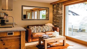 A cozy living area with a stone wall, a wooden ceiling, a leather sofa with decorative pillows, a coffee table with candles, and a large window offering a view of the outdoors. - Casa Jacuzzi Appartement/Fewo, Bad, WC, 4-Bettwohnung by Interhome (Arosa)