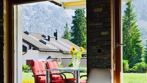 A room with a glass door leading to a patio with red chairs, a glass table, and a vase with sunflowers. - Casa Jacuzzi Appartement/Fewo, Bad, WC, 4-Bettwohnung by Interhome (Arosa)