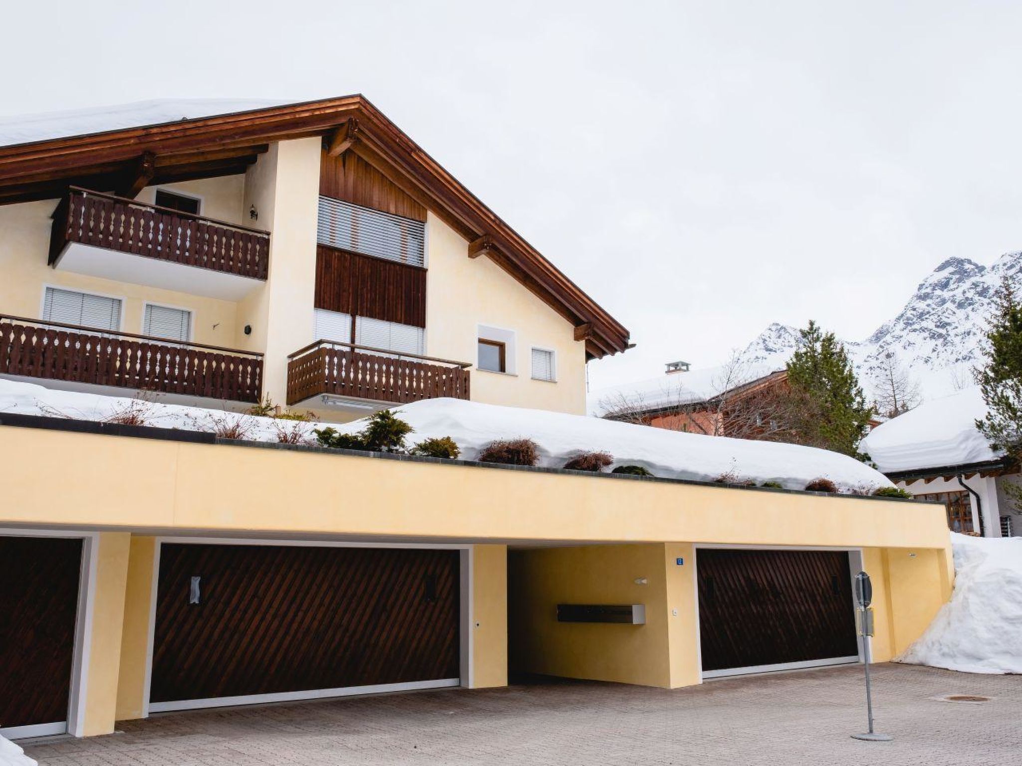 Ein mehrstöckiges Gebäude mit Balkon, Garage und einem mit Schnee bedeckten Dach.