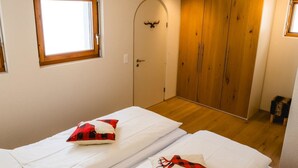 A bedroom with two beds, a wooden wardrobe, a door with a deer head decoration, and a window. - Casa Jacuzzi Appartement/Fewo, Bad, WC, 4-Bettwohnung by Interhome (Arosa)