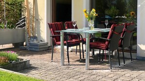 An outdoor patio with a glass table, red upholstered chairs, and a vase with sunflowers. - Casa Jacuzzi Appartement/Fewo, Bad, WC, 4-Bettwohnung by Interhome (Arosa)