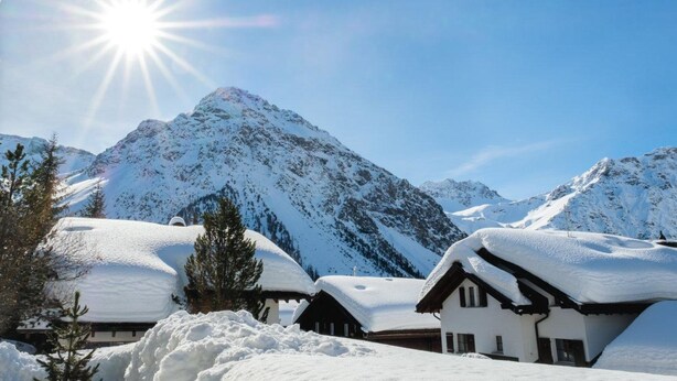 A snow-covered mountain landscape with a bright sun, and several chalet-style buildings with snow-covered roofs. - Casa Jacuzzi Appartement/Fewo, Bad, WC, 4-Bettwohnung by Interhome (Arosa)
