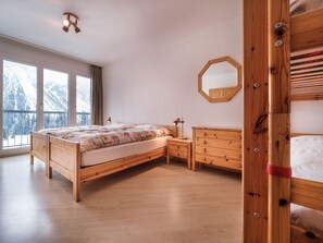 A bedroom with a wooden bed, a nightstand, a dresser, a mirror, and a window with a view of snow-covered mountains. - Bristol 41 Appartement/Fewo, Dusche oder Bad, WC, 4-Bettwohnung by Interhome (Arosa)