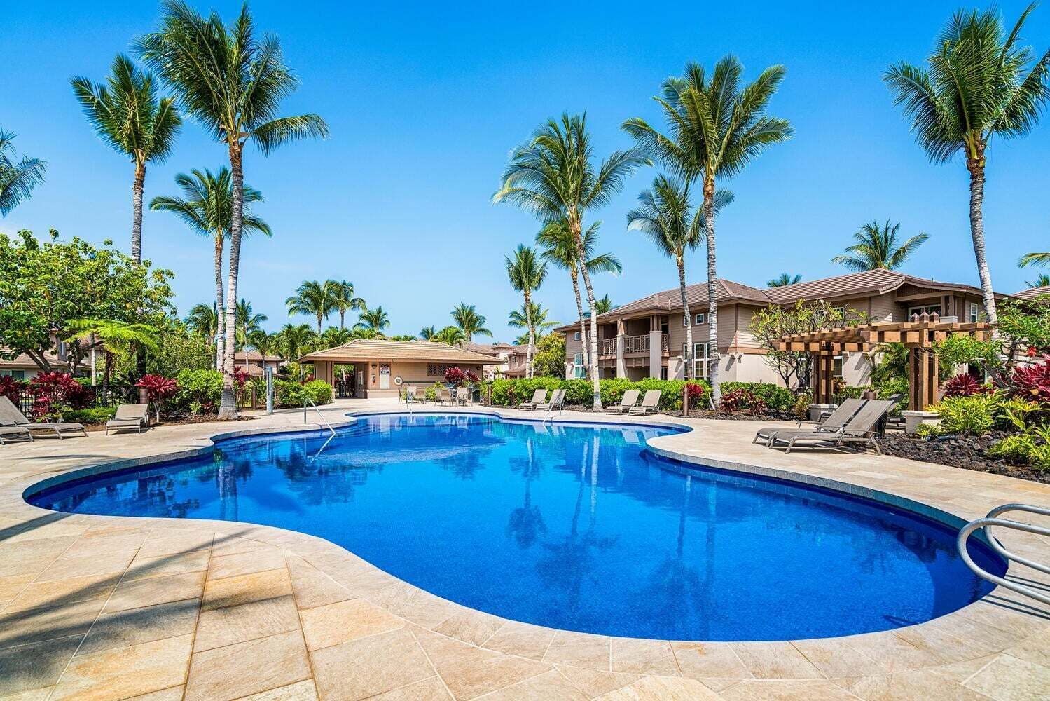 Ein Swimmingpool mit Liegestühlen, Palmen und einem Gebäude mit einem Ziegeldach.