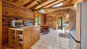 Interior de una cabaña de madera con cocina, mesa de comedor de madera y un refrigerador.