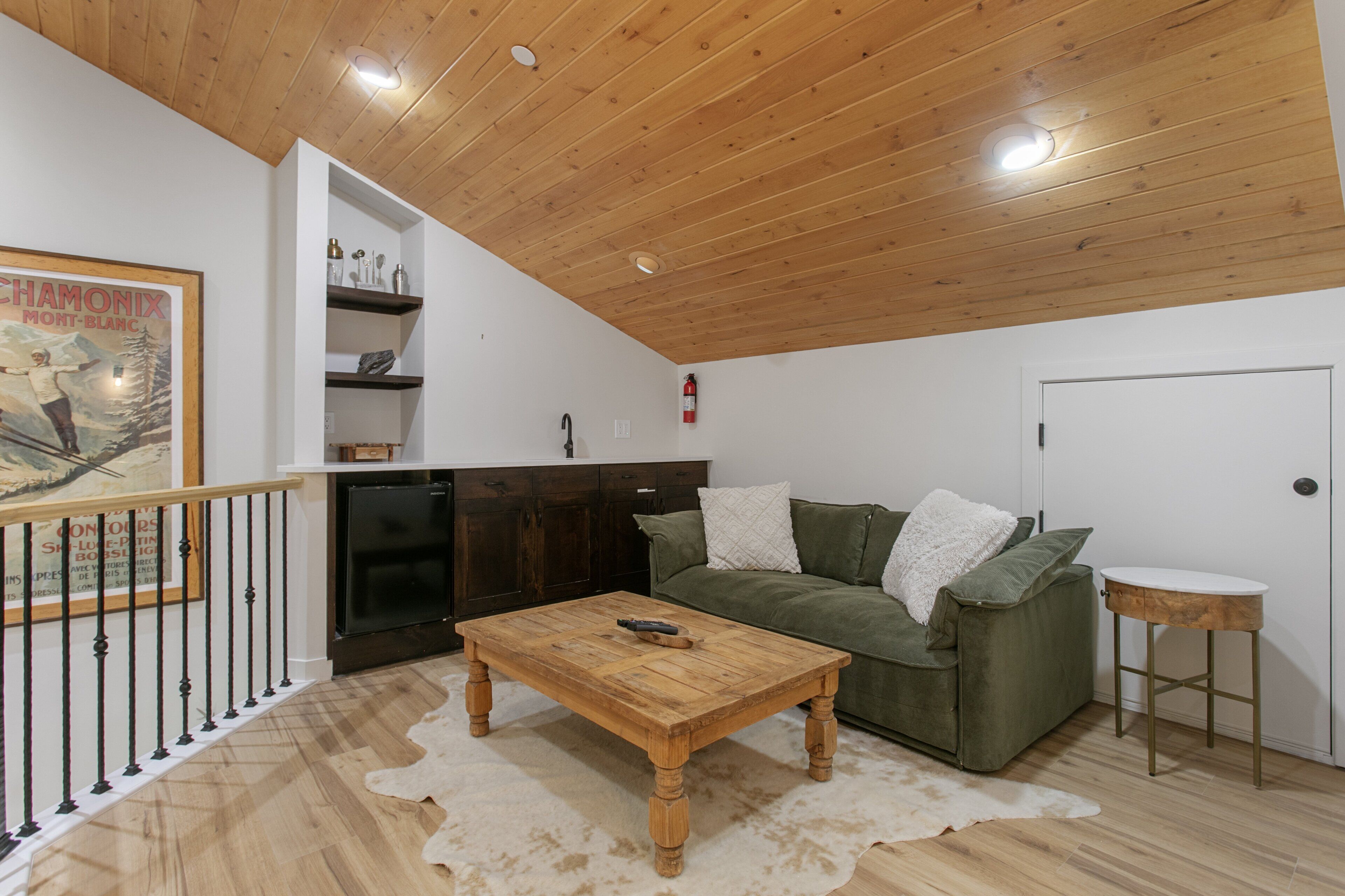 A living room with a wooden ceiling, a green sofa, a wooden coffee table, and a white rug.