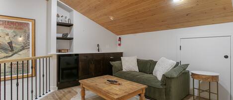 A living room with a wooden ceiling, a green sofa, a wooden coffee table, and a white rug.