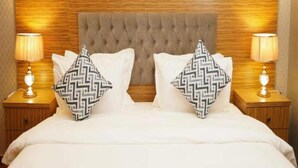 Een bed met een gestoffeerd hoofdeinde, twee bedlampen en decoratieve kussens.