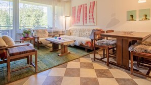 A cozy living room with a sofa, chairs, a coffee table, and a dining table. There are large windows with curtains, a lamp, and artwork on the wall. - Rothornblick 11 by Arosa Holiday Appartement/Fewo, Bad, WC Rothornblick 11 by Interhome (Arosa)