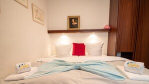 A hotel room with a bed, pillows, a red accent pillow, and towels with a logo. - Rothornblick 11 by Arosa Holiday Appartement/Fewo, Bad, WC Rothornblick 11 by Interhome (Arosa)