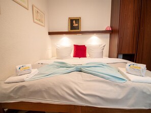 A hotel room with a bed, pillows, a red accent pillow, and towels with a logo. - Rothornblick 11 by Arosa Holiday Appartement/Fewo, Bad, WC Rothornblick 11 by Interhome (Arosa)