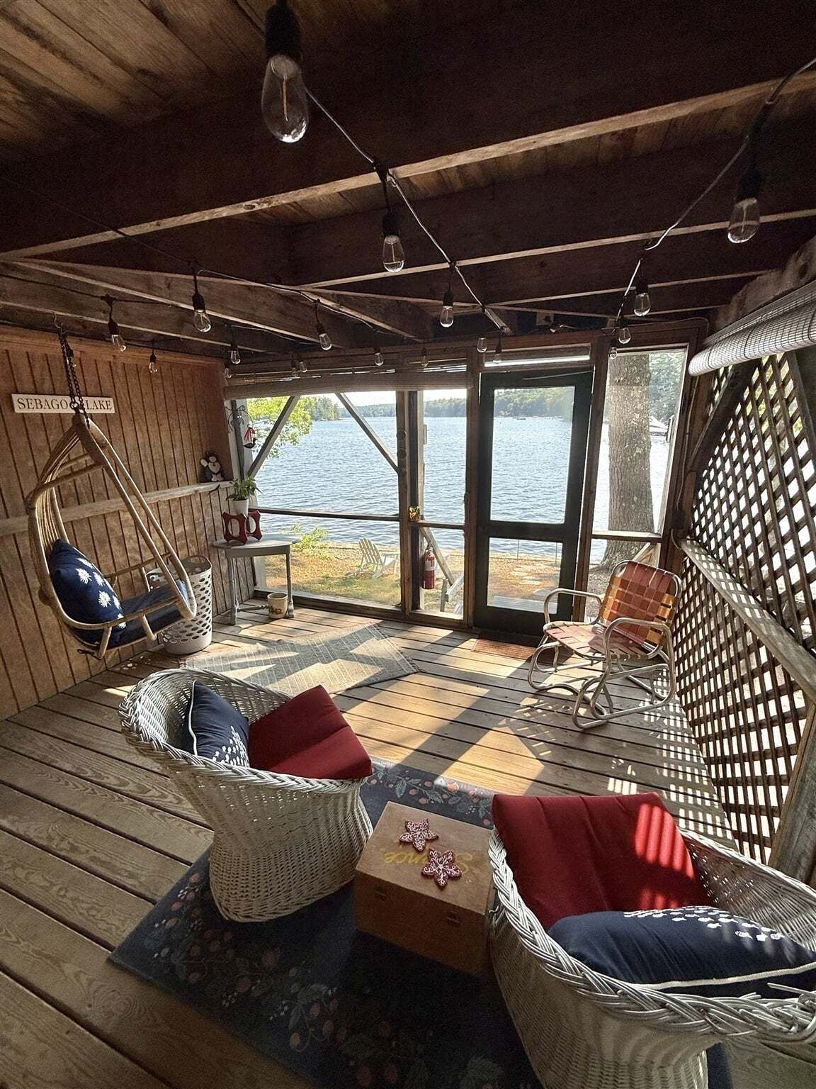 Eine Holzhütte mit Korbmöbeln, einem Hängesessel und Blick auf einen See.