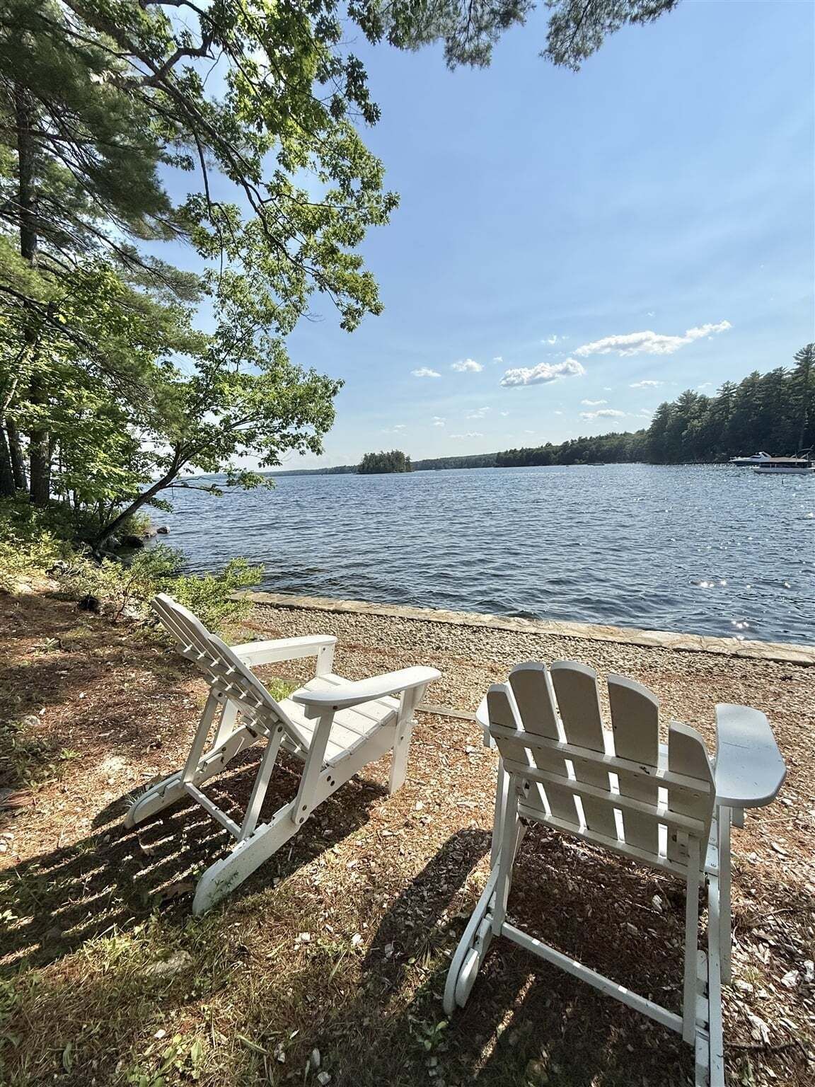Two Adirondack chairs by a lakeside with a view of the water and trees.