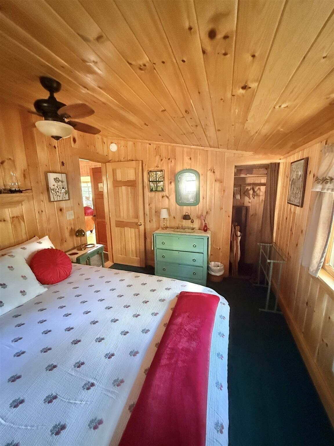 A wooden-paneled room with a bed, dresser, and a ceiling fan.