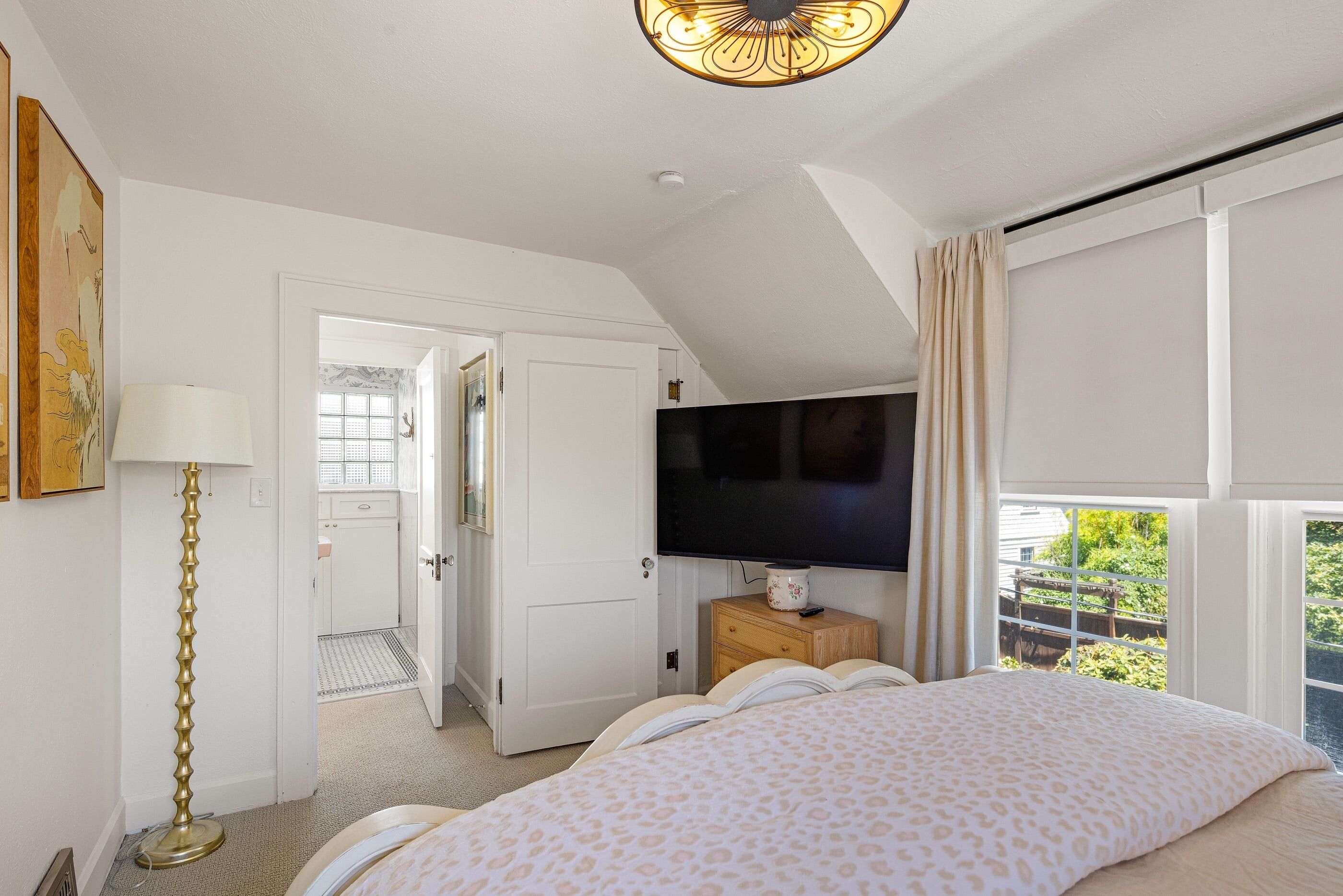 Une chambre à coucher comprenant un lit, une télévision, une table de chevet, une lampe et une fenêtre donnant sur un beau paysage.