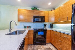 Eine Küche mit Holzausstattung, einer Edelstahlspüle, einer Mikrowelle, einem Backofen und einer Kaffeemaschine.