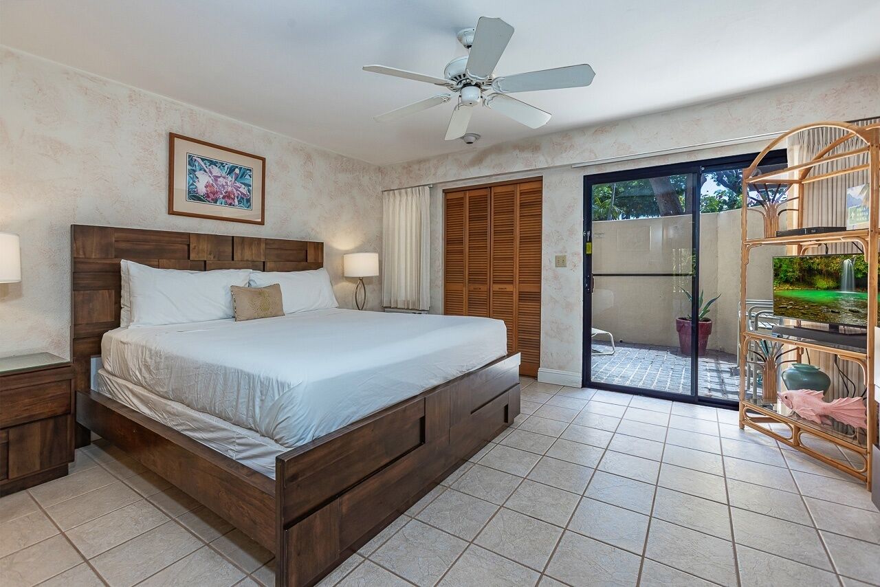 Une chambre dotée d’un grand lit, d’un ventilateur de plafond, d’une porte-fenêtre coulissante donnant sur un balcon et d’un petit coin où sont exposées des plantes d’intérieur.